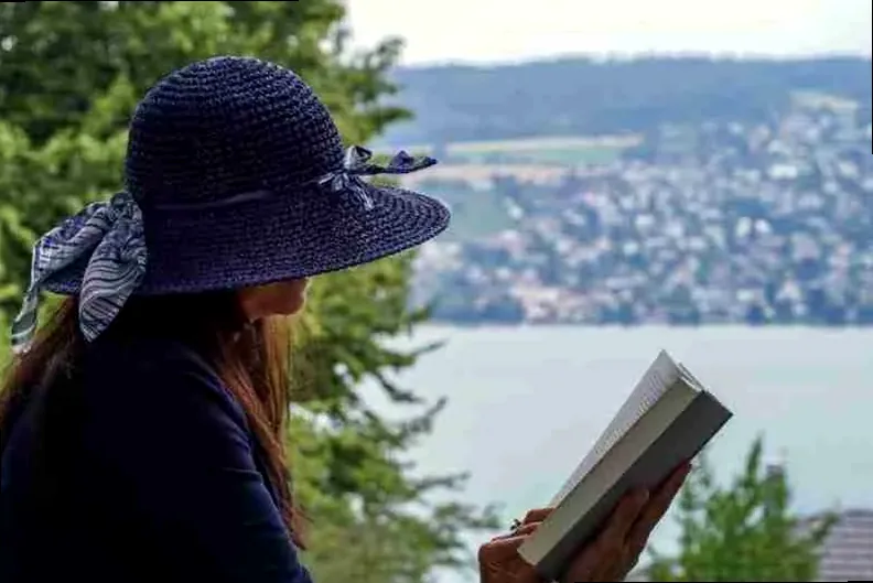 A woman sitting by a lake, reading a book